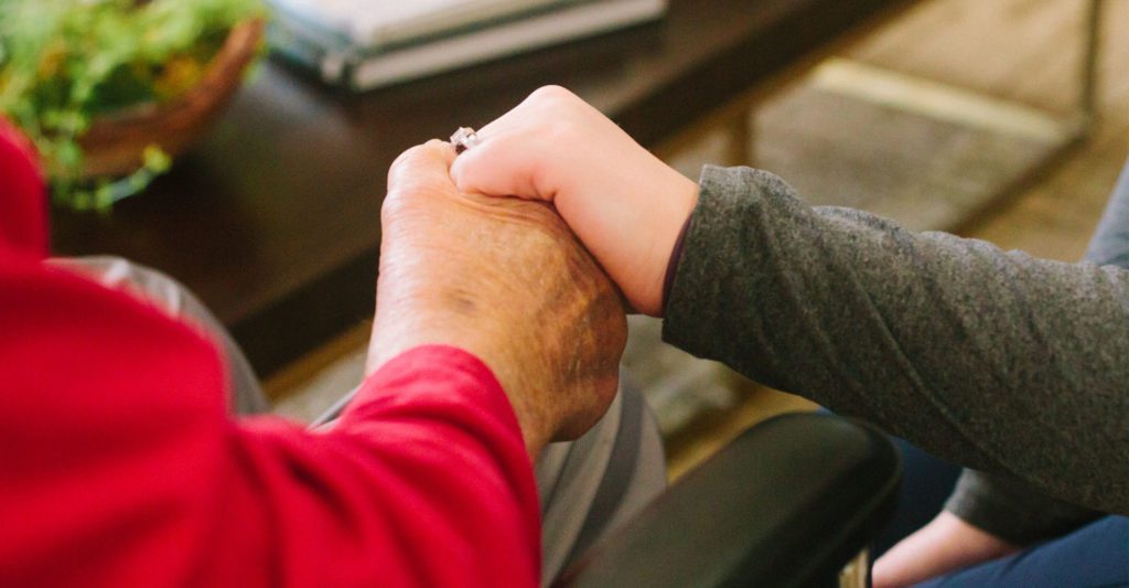 A nurse and patient at a skilled nursing facility holding hands